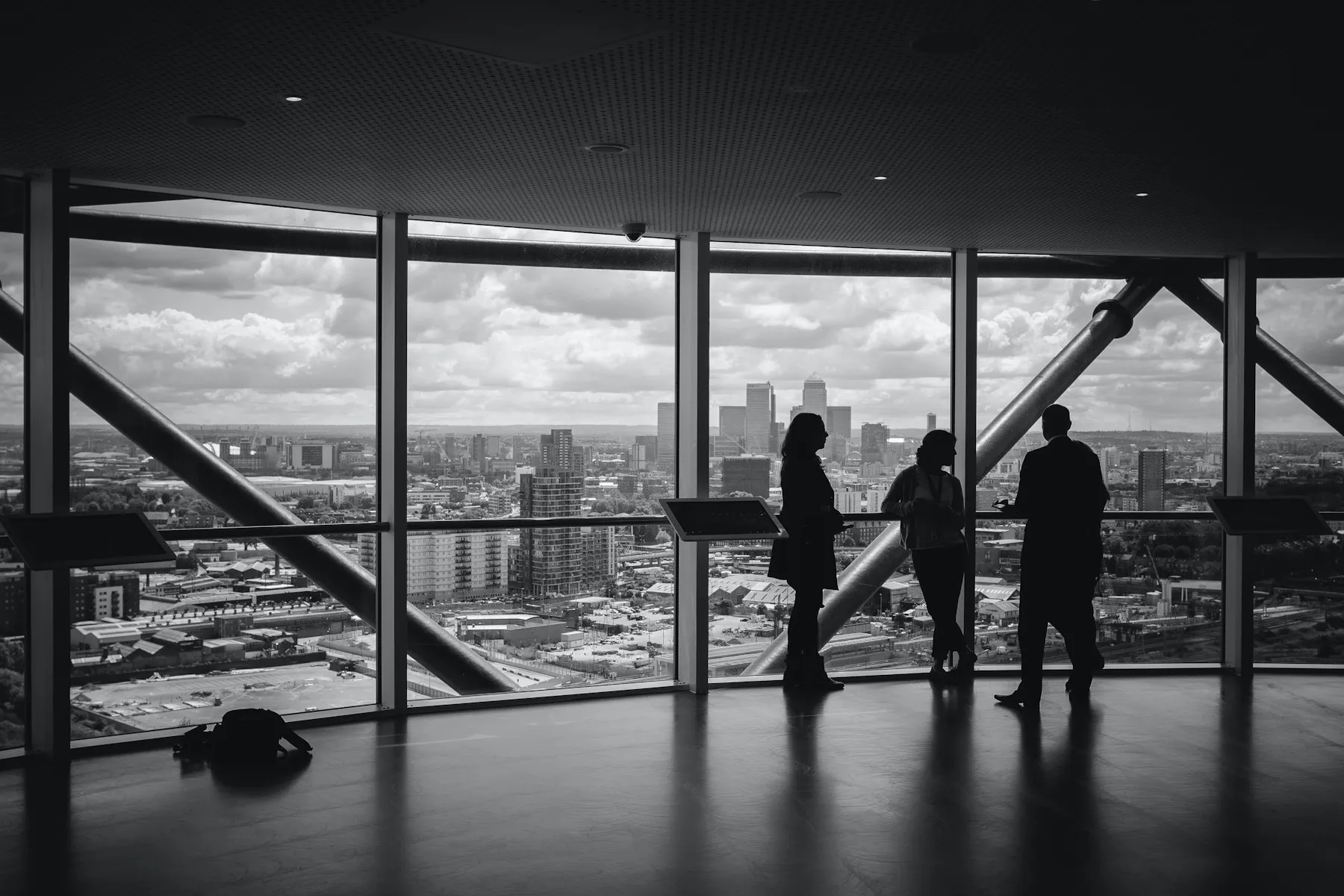 Silhouettes of three people meeting near a floor-to-ceiling window overlooking a city skyline