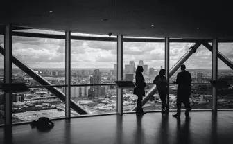 Silhouettes of three people meeting near a floor-to-ceiling window overlooking a city skyline