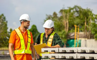 Two workers in safety vests reviewing plans on an industrial site