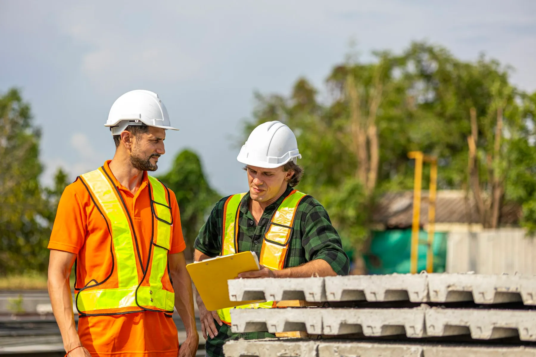 Two workers in safety vests reviewing plans on an industrial site