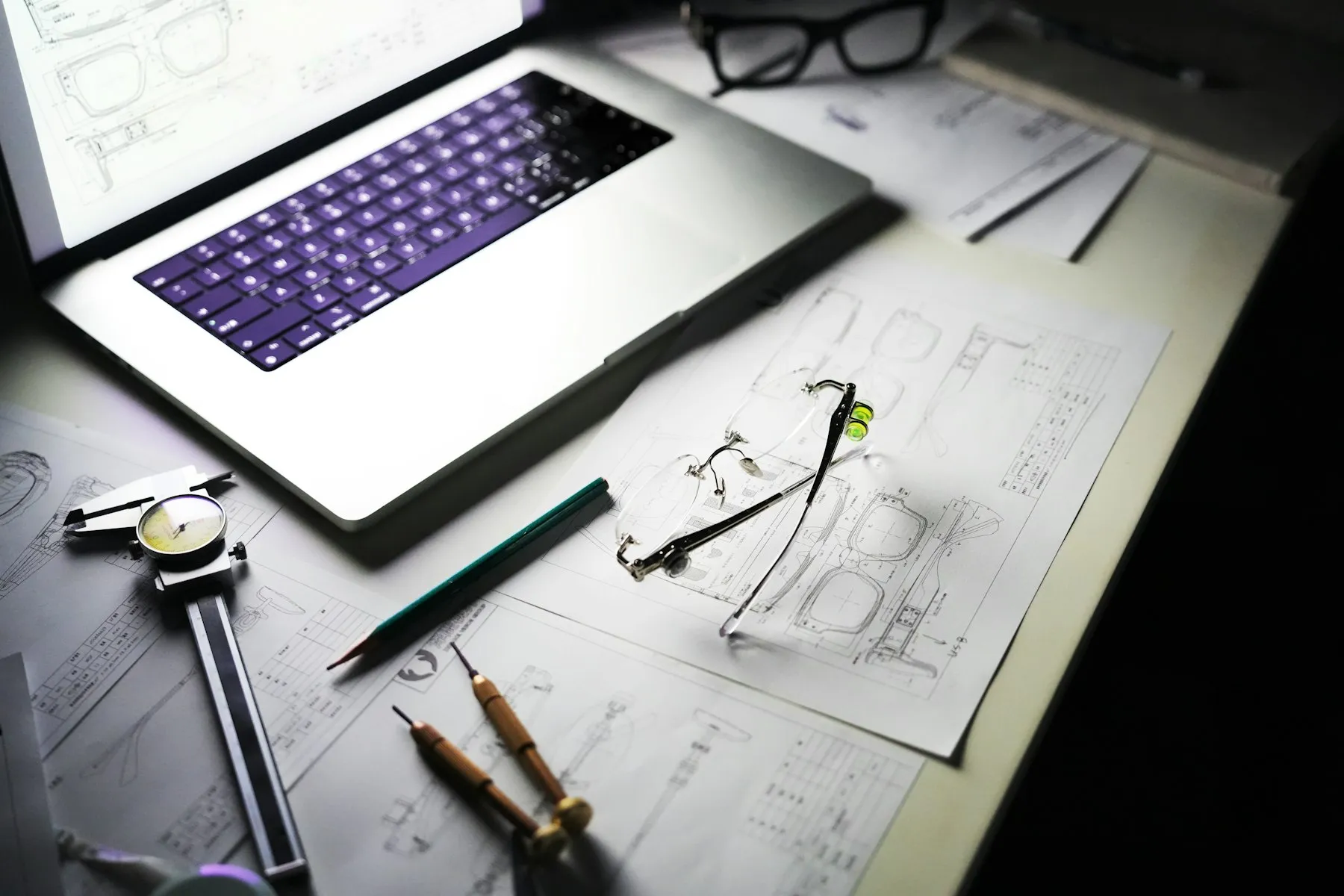 A product design desk with a laptop, technical drawings, and tools