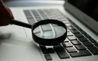 A hand holding a magnifying glass over a laptop keyboard