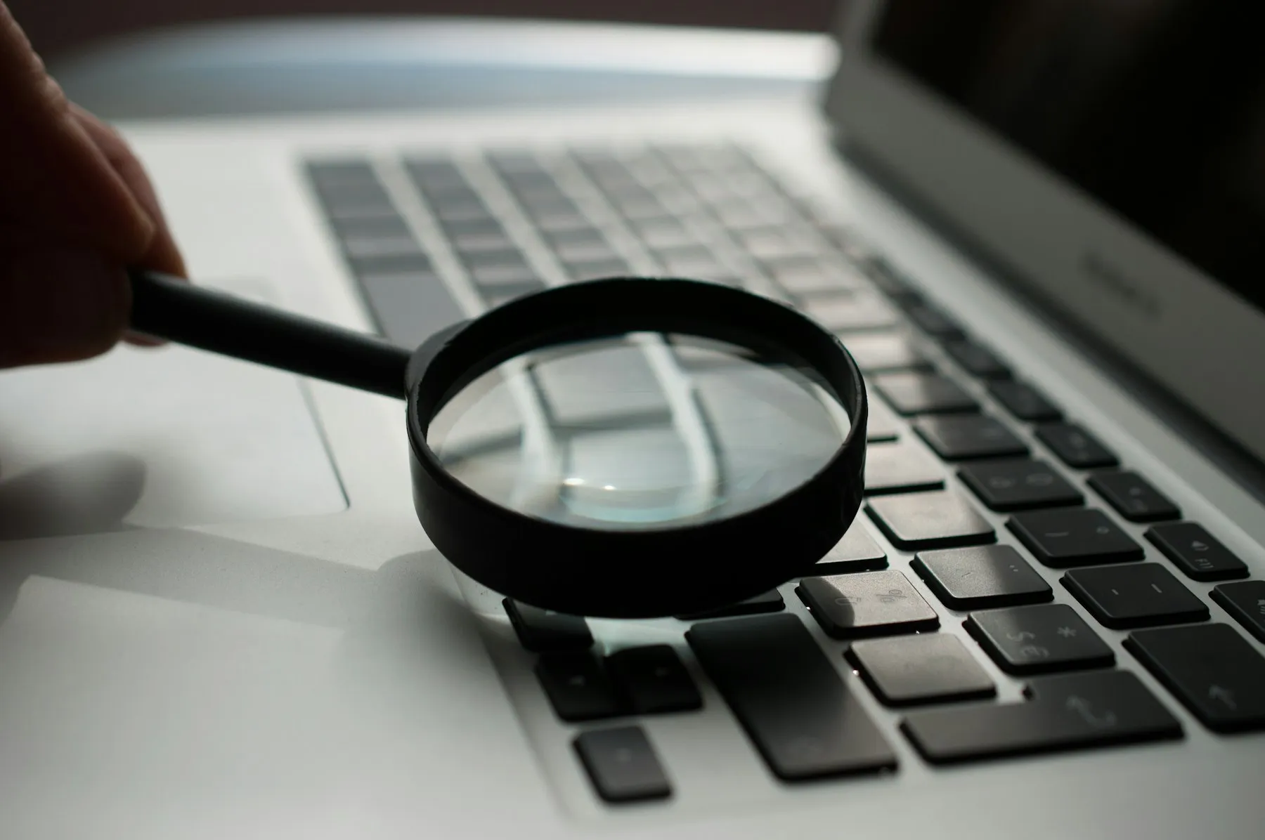 A hand holding a magnifying glass over a laptop keyboard
